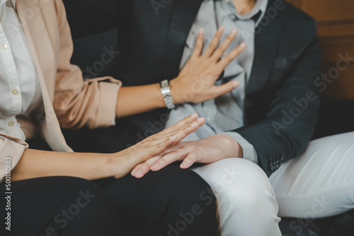 Unhappy asian young employee woman defending at hand of colleagues, man or boss touching her knee feeling disgusted and uncomfortable. Sexual harassment inappropriate at office, workplace concept. photo