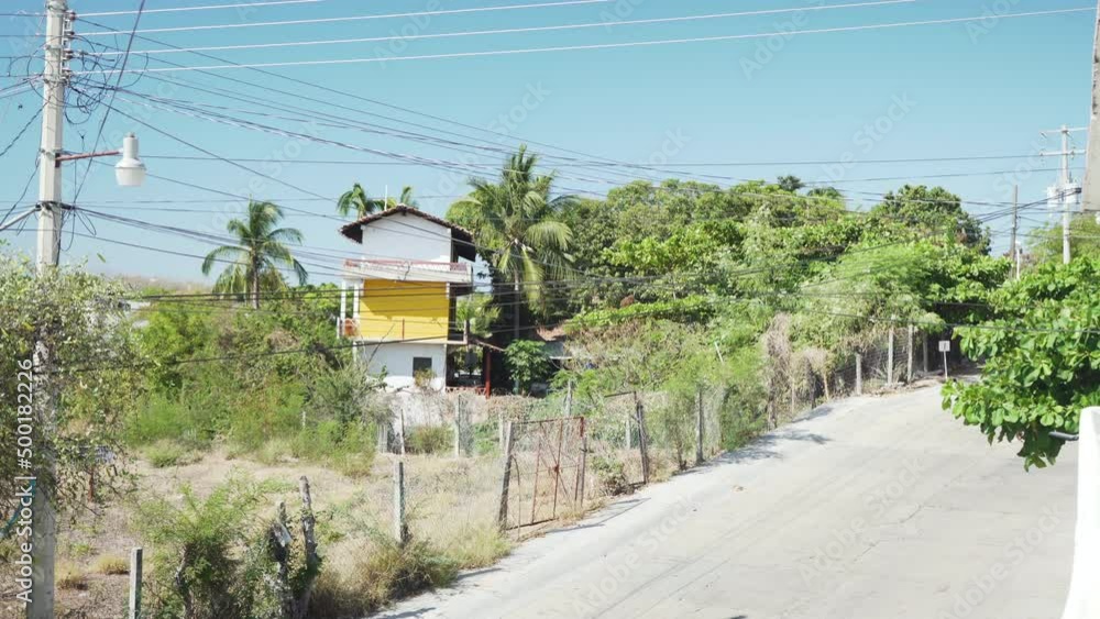 A remote dusty dirt track road in Puerto Escondido, on the Oaxaca coast in Mexico. With a house, big green trees and telephone lines. A remote dusty dirt track road in Puerto Escondido, on the Oaxaca coast in Mexico. With a house, big green trees and telephone lines.