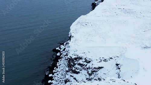 White snow covered cliffs along calm ocean water, Iceland, aerial photo