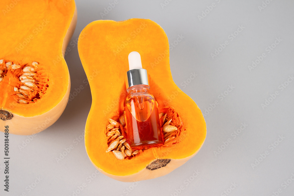 Orange dropper bottle with natural organic pumpkin seeds cosmetic oil - natural oil extract for skincare or hair with pumpkins. Beauty treatment, natural herbal cosmetics concept. Selective focus
