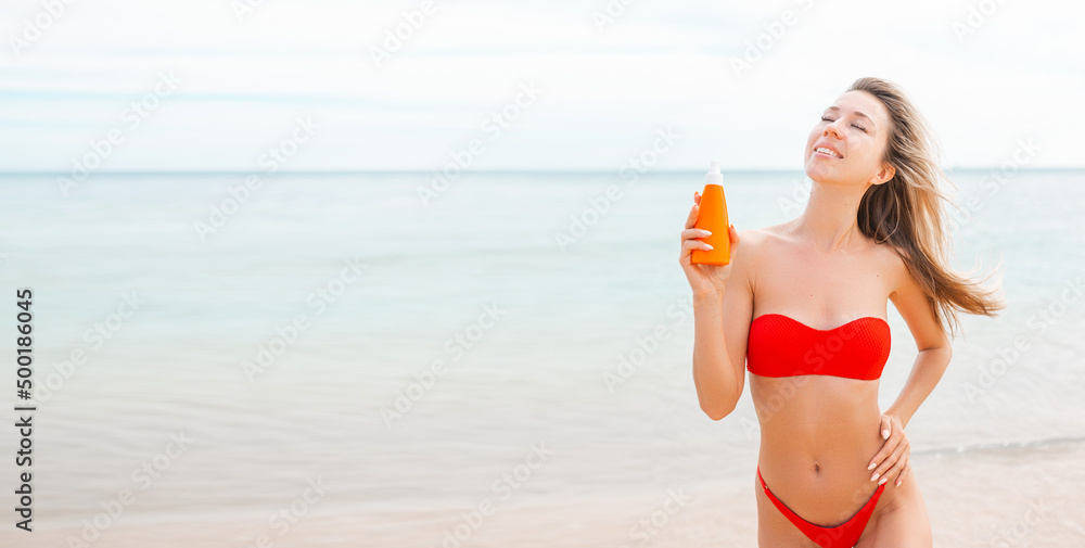 Woman applying sun cream on tanned body In form heart love to protect her skin. Girl using sunscreen. Female holding suntan lotion, moisturizing sunblock on sunny day with blurry sea in the background