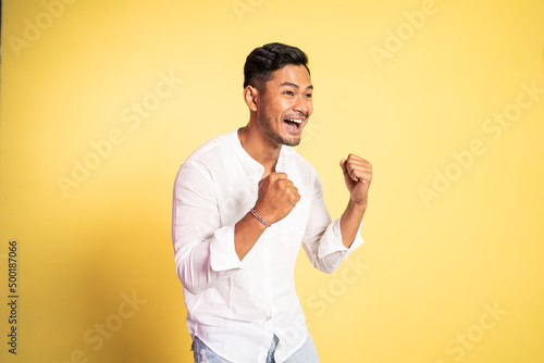 excited asian young man with two fists clenched on isolated background
