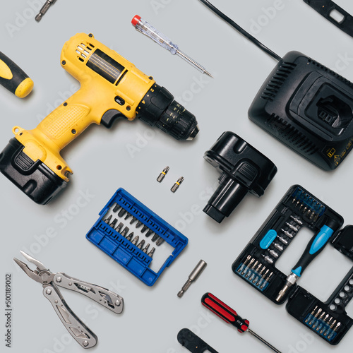 DIY home tool minimal concept. Pattern made of yellow cordless drill, battery charger, tool kits, screwdrivers, stainless multi pliers. Flat lay arrangement gray background