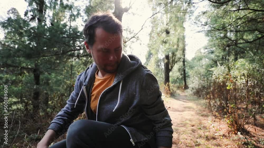 Young man sits in a forest taking a break during hiking with sunlight in the back Young man sits in a forest taking a break during hiking with sunlight in the back