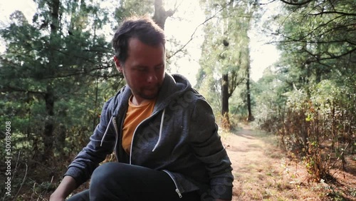 Young man sits in a forest taking a break during hiking with sunlight in the back