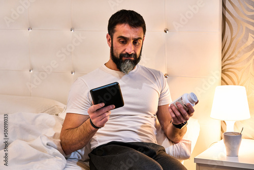 man who can't sleep with doubts between reading an ebook or taking the medicine he has in a bottle of pills