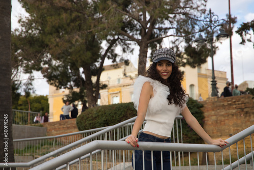 Young and beautiful woman, brunette, with curly hair, with a nice smile, wearing a white shirt, jeans and cap, leaning on a railing. Concept beauty, fashion, model, trend, happiness.
