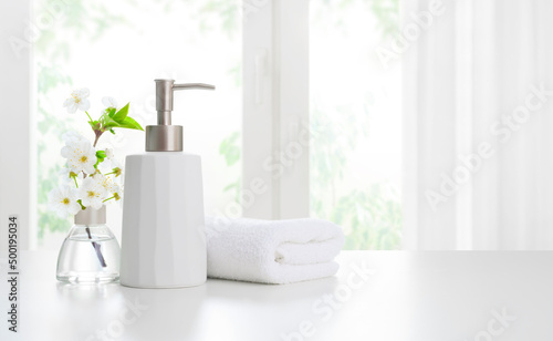 Soap dispenser with towels and aromatic flowers on light background