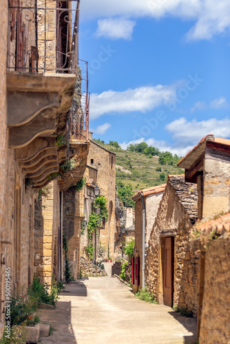 Narrow light streets of Peyre village with limestone buildings of different eras with decorated balconies. Aveyron  Occitania  Southern France