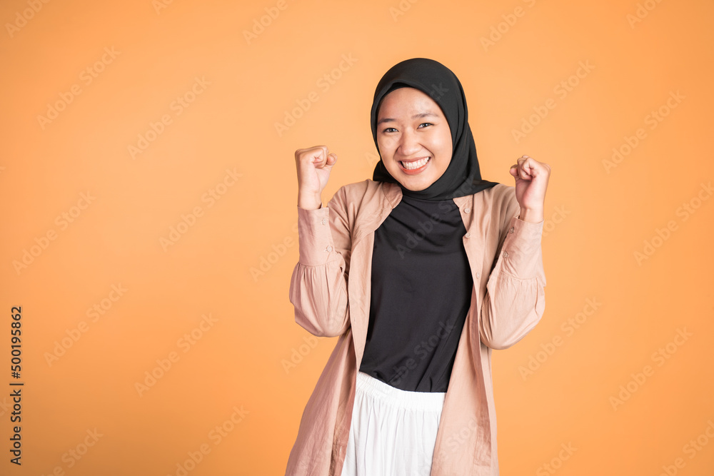 Excited young woman in hijab clenching hands while celebrating success on isolated background Excited young woman in hijab clenching hands while celebrating success on isolated background