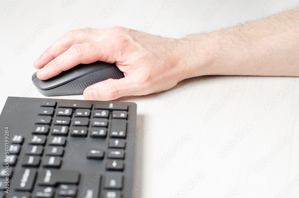 A computer mouse in a man's hand and a black keyboard. White background. A computer mouse in a man's hand and a black keyboard. White background.