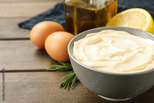 Bowl with fresh mayonnaise and ingredients on wooden table, closeup. Space for text photo