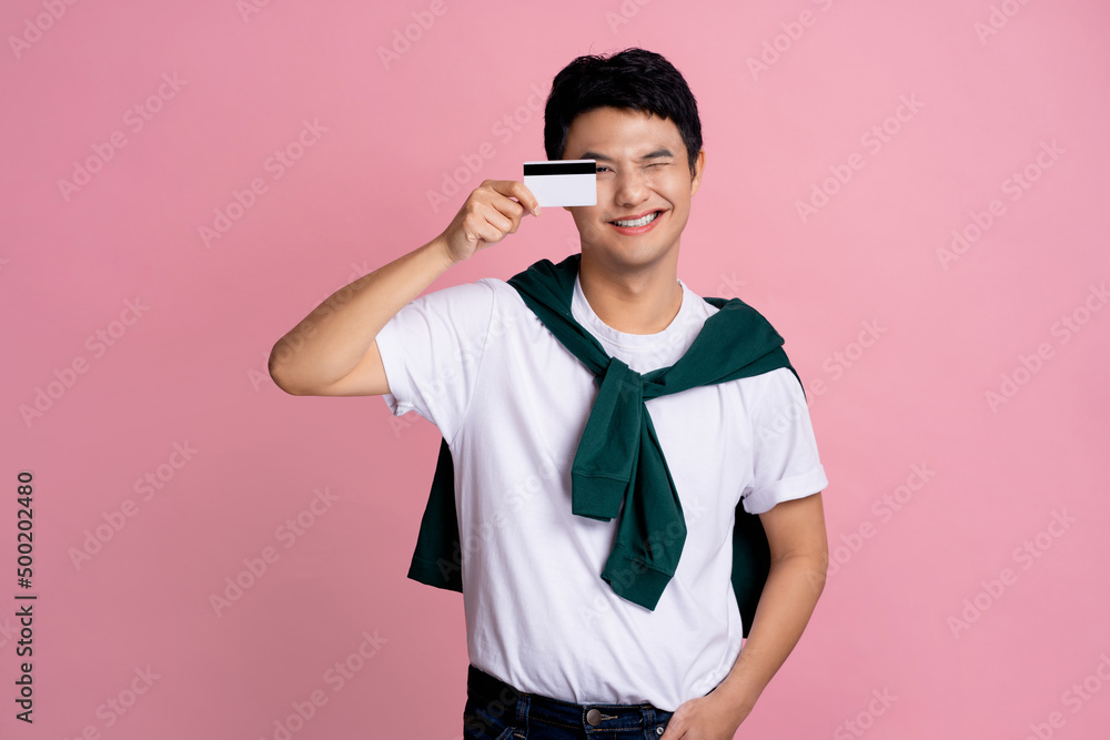 Smiling handsome young man in casual clothes posing alone on a pink wall photo studio background. He holds a bank card Smiling handsome young man in casual clothes posing alone on a pink wall photo studio background. He holds a bank card
