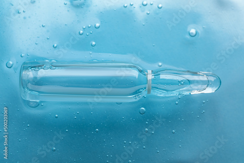Pharmaceutical ampoule with medication in transparent gel on light blue background, closeup
