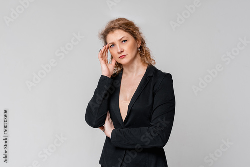 Businesswoman having her hand on her head while looking dejected, standing in suit over light grey background. Successful businesswoman leading business