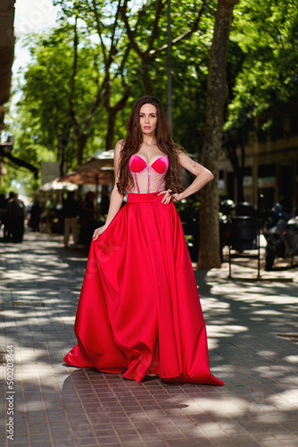 Attractive beautiful girl in a red dress standing on the city