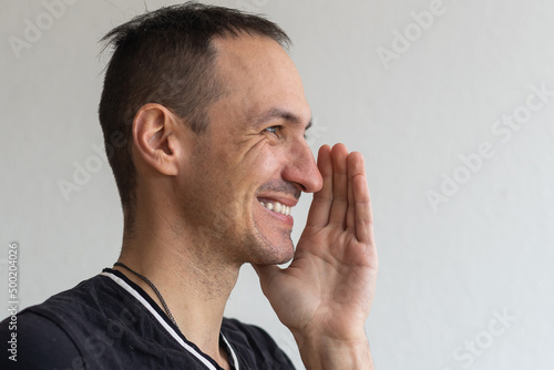 Positive smiling man with beard holding finger near lips showing shh gesture, keeping secrets preparing surprise. Indoor studio shot isolated on white background.