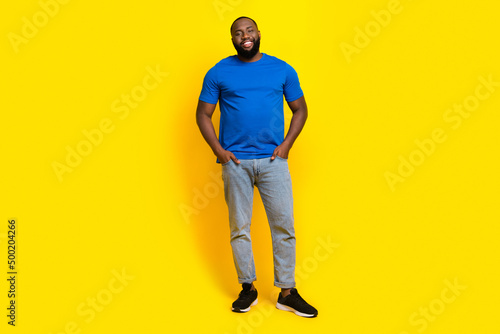 Full length body size view of attractive cheerful guy holding hands in pockets isolated over bright yellow color background