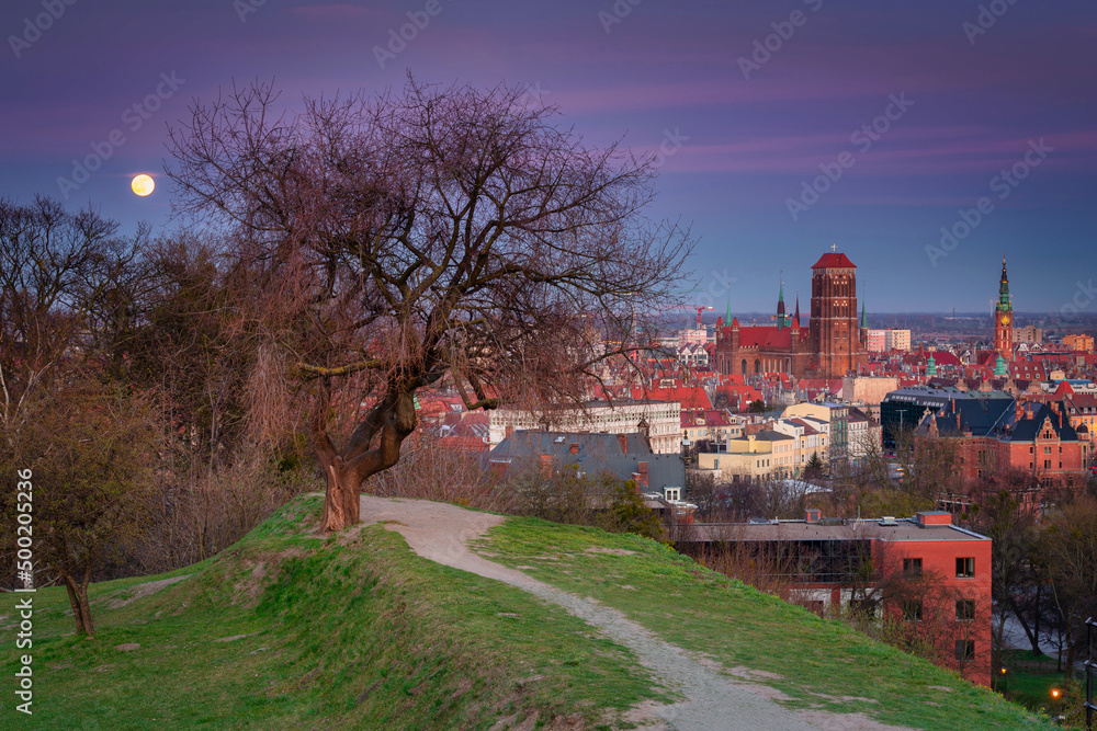 Fototapeta premium Beautiful cityscape of Gdansk with St. Mary Basilica and City Hall at dusk with the full moon, Poland.