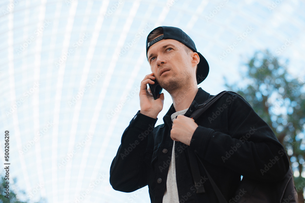 young fashionable modern guy, a man in a black cap and sunglasses with a smartphone, talks on the phone on a city urban background in a tunnel in the sunset rays of the sun. young fashionable modern guy, a man in a black cap and sunglasses with a smartphone, talks on the phone on a city urban background in a tunnel in the sunset rays of the sun.