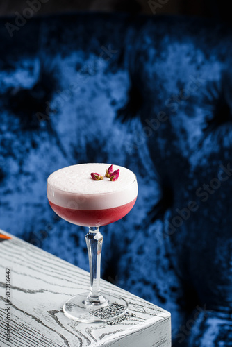 Pink Clover Club Cocktail in Coupe Glass with Layer of Foam and flower Garnish isolated on dark Background