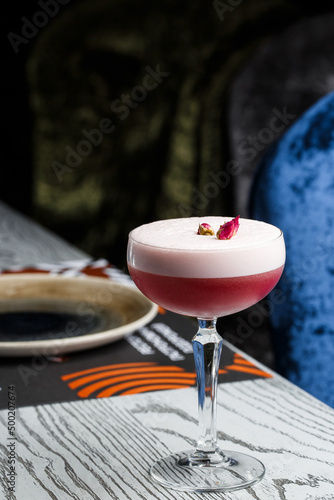 Pink Clover Club Cocktail in Coupe Glass with Layer of Foam and flower Garnish isolated on dark Background