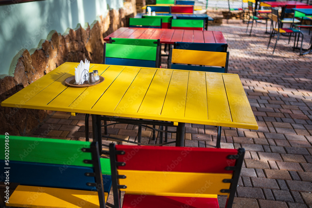 colorful wooden tables and chairs in a cafe on the street terrace in the park.
