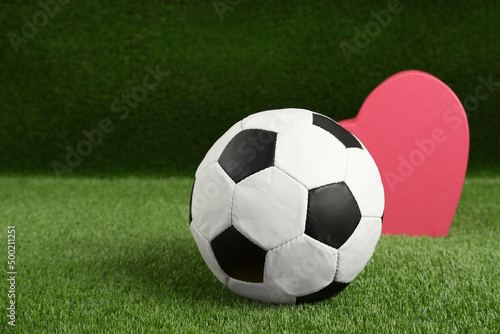 Soccer ball and heart on green grass. Space for text