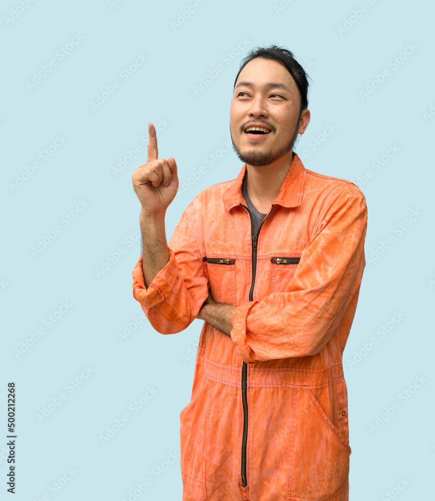 The chief mechanic in an orange uniform pointing one finger in upward direction. Portrait on blue background with studio light.