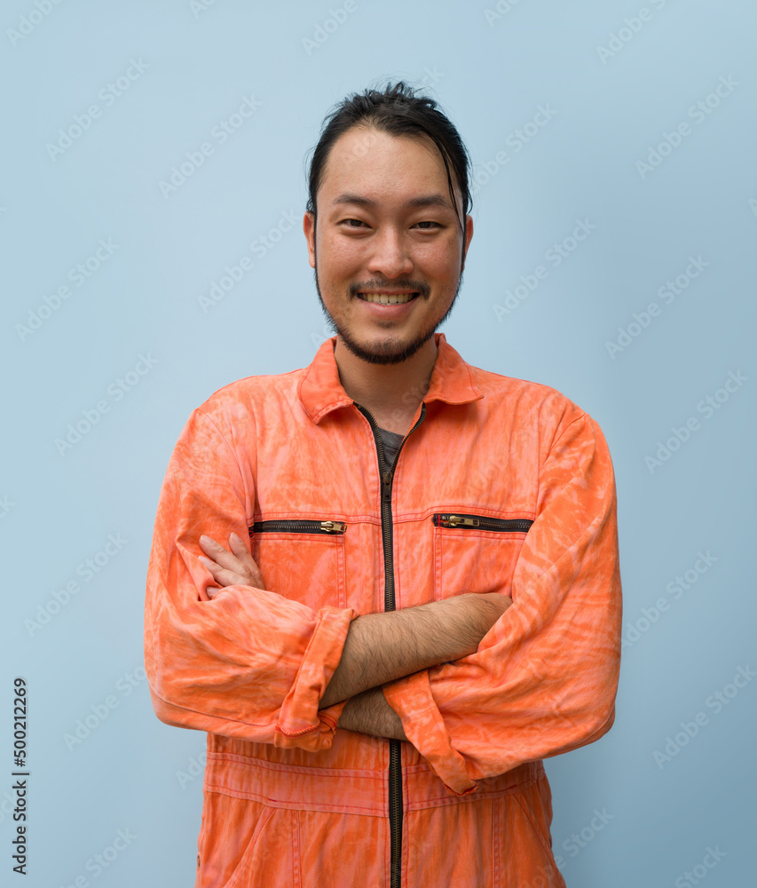 Young long hair asian man with mustache and beard stand smiling with his arms crossed. Portrait of industrial people on blue background. Young long hair asian man with mustache and beard stand smiling with his arms crossed. Portrait of industrial people on blue background.