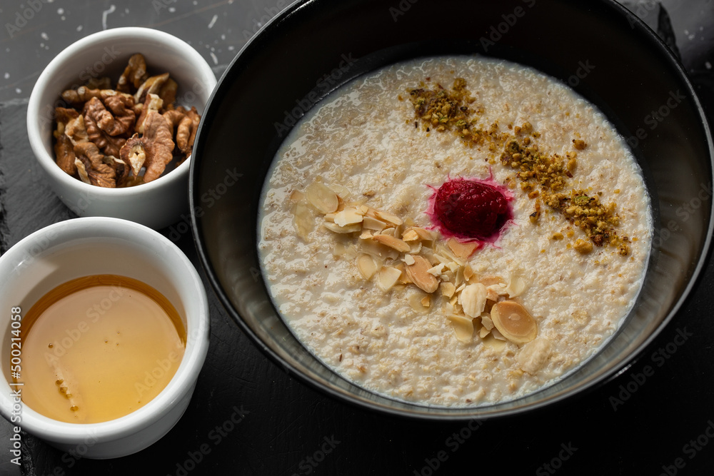 Semolina porridge for breakfast oat with nuts in black bowl served with honey isolated on black stone background. Homemade food. Tasty breakfast.