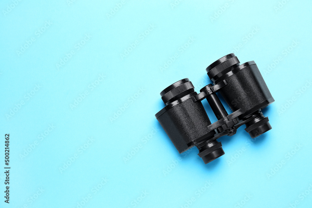 Modern binoculars on light blue background, top view. Space for text Modern binoculars on light blue background, top view. Space for text
