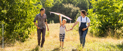 Happy family with pregnant wife fly a kite together in summer field
