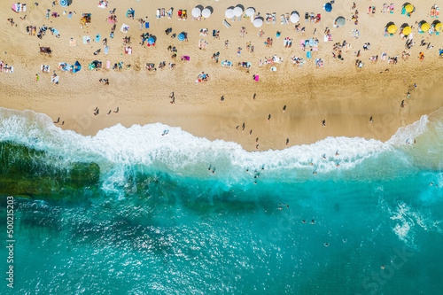 aerial shooting from a drone on a sandy beach with people sunbathing and relaxing. Flat view of the shore and turquoise waves of the surf and people bathing
