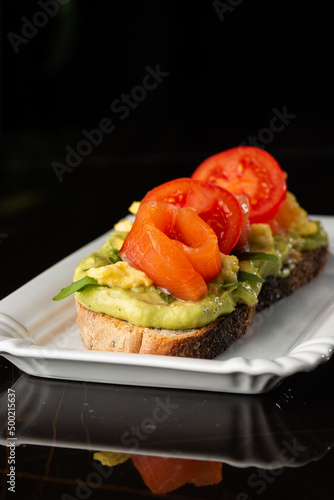 Buckwheat bread toast with an egg, a sliced avocado, a salmon, tomatoes and lettuce. Dietary menu. Flat lay.