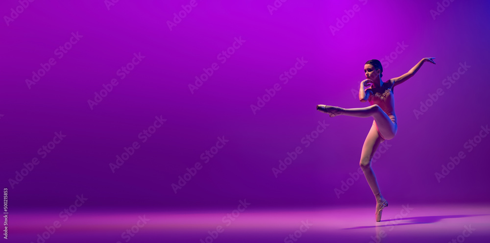 Portrait of young little ballet dancer, teen jumping isolated on purple background in neon light. Art, grace, beauty, ballet school concept