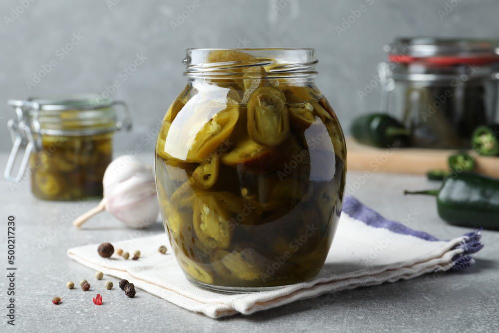 Glass jar with slices of pickled green jalapeno peppers on light grey table Glass jar with slices of pickled green jalapeno peppers on light grey table
