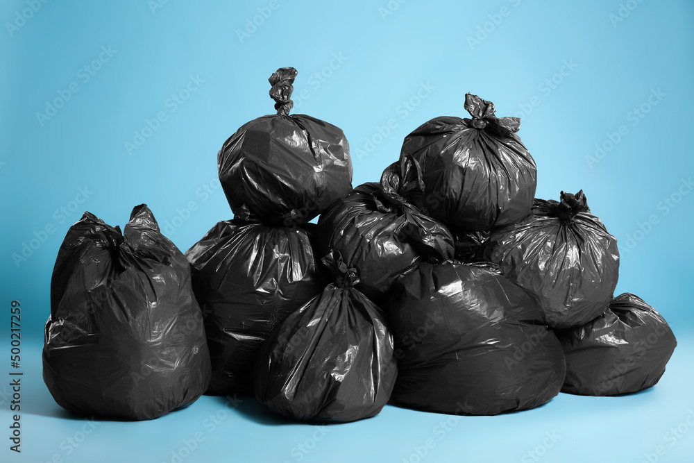 Black trash bags full of garbage on light blue background Black trash bags full of garbage on light blue background