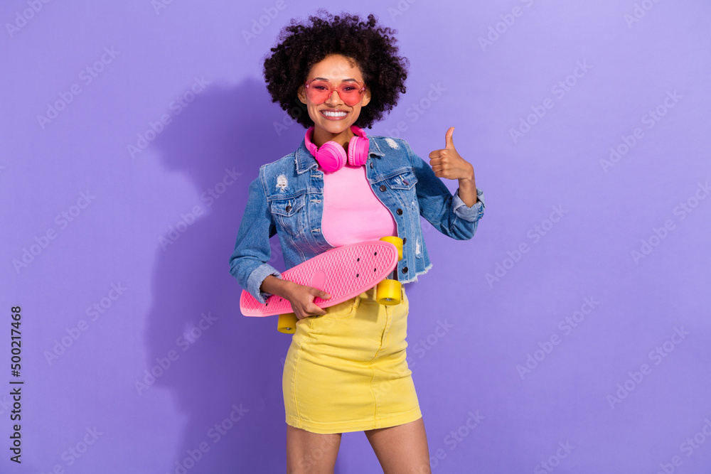 Photo of funky confident young lady dressed denim jacket earphones long board thumb up isolated purple color background Photo of funky confident young lady dressed denim jacket earphones long board thumb up isolated purple color background