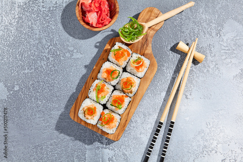 Maki roll with salmon tartare top and tobiko on wooden board in contemporary composition. Sushi roll with chopsticks on concrete table. Maki sushi in minimal style.