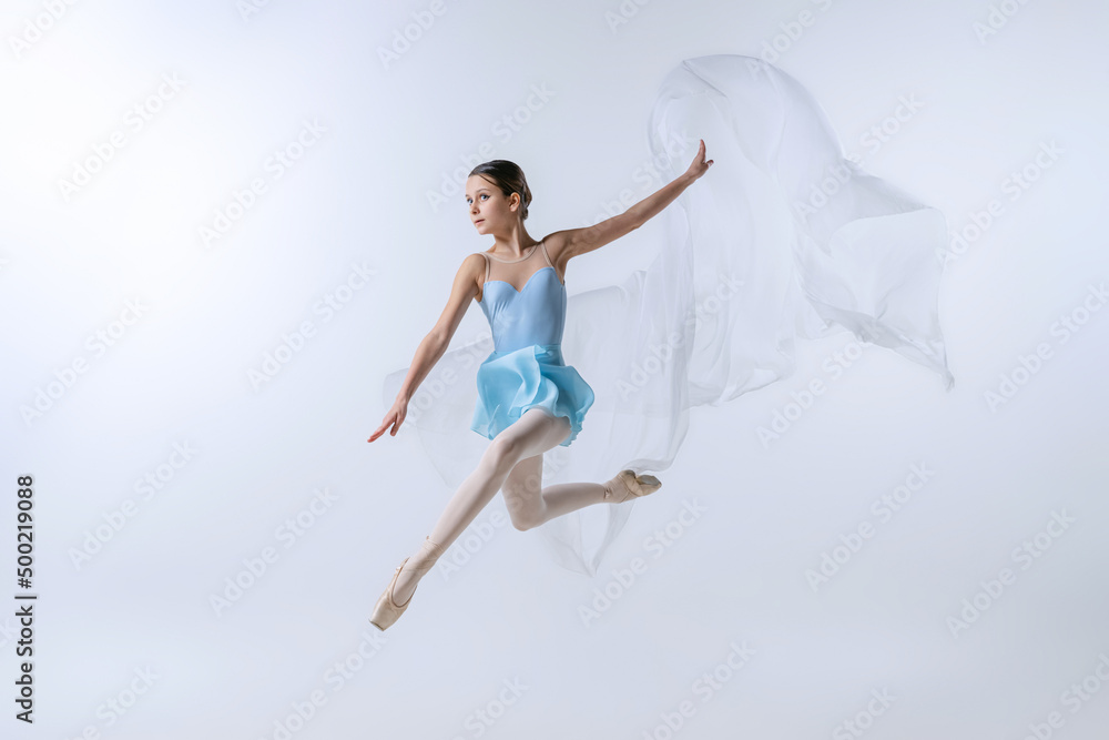 One young girl, aspiring ballerina in blue dress and pointes dancing with cloth isolated on gray background. Art, grace, beauty, ballet school concept