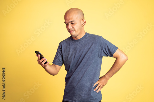 bald asian man angry while looking at mobile phone on isolated background © Odua Images