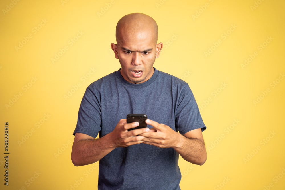 bald asian man shocked while looking at smartphone on isolated background bald asian man shocked while looking at smartphone on isolated background