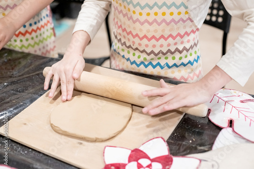 child potter rolls a brown clay with rolling pin on a special board on a wooden table to make a plate.Pottery workshop.Pottery workshop. teaching schoolchildren. hobbies and leisure for children.