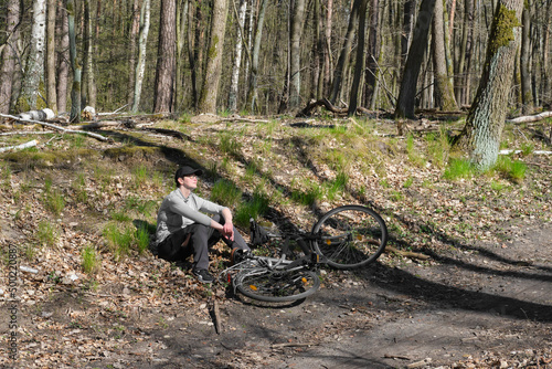 Female biker resting next to her bicycle in Spring forest. Country road, bike way, foot path through Spring greenery. Springtime forest, romantic footpath on a sunny day in April. Staycation mode on. photo
