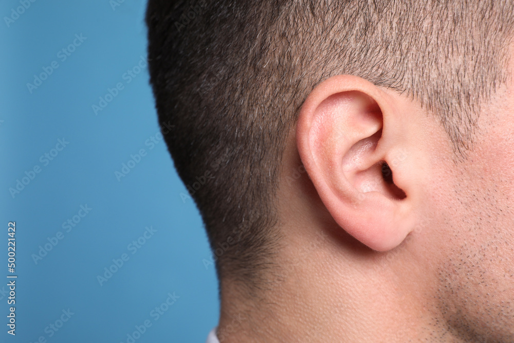 Man on light blue background, closeup of ear. Space for text Man on light blue background, closeup of ear. Space for text