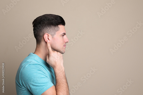 Man pointing at his ear on beige background. Space for text