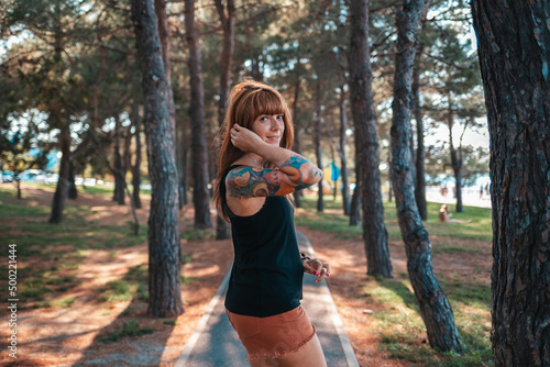Caucasian young smiling woman with a tattoo on her arm is walking in the park and look around. Summertime concept