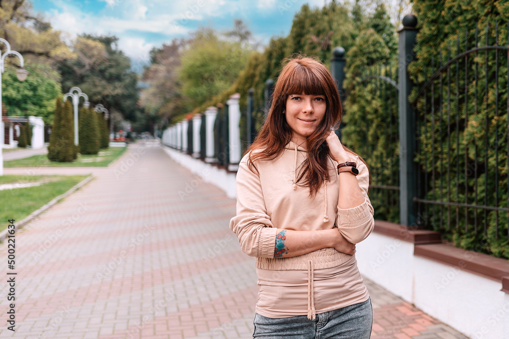 Portrait of a young smiling woman with her tattoed arms posing at the street. The concept of successful confident people Portrait of a young smiling woman with her tattoed arms posing at the street. The concept of successful confident people
