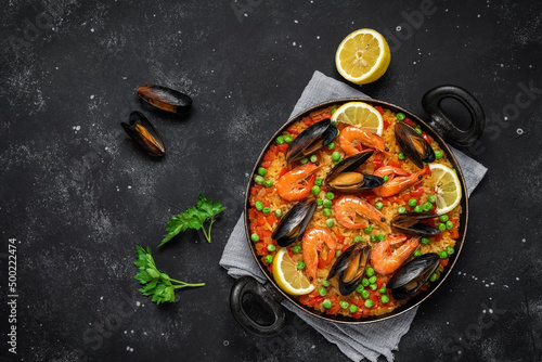 Fotografie, Obraz Traditional Spanish paella with seafood in a frying pan on a black stone background